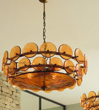 Looking up at an amber disc chandelier from Clérachic in a room with a stone wall, the textured bowl glowing underneath.