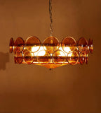 Amber glass disc chandelier from Clérachic lit bright, with the bulbs showing through the discs against a copper-brown wall.