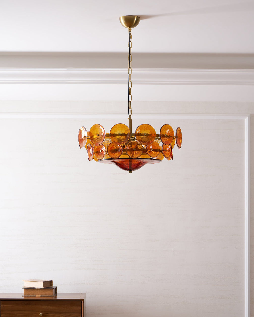 Small amber disc chandelier from Clérachic hanging in a white panelled room above a dark wood sideboard.