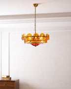 Amber chandelier from Clérachic, lit, in a white room with a wooden sideboard and a stack of books at the left.