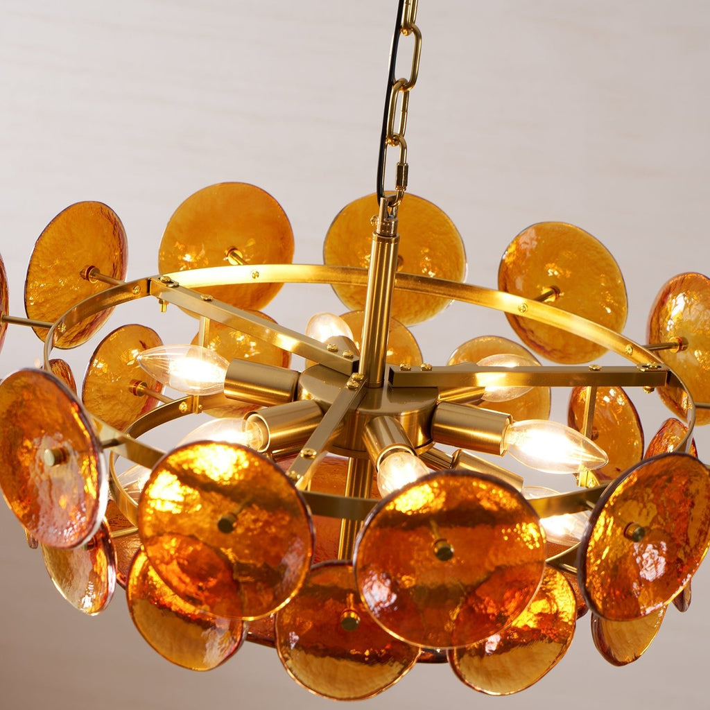 Close view from below of lit amber discs and candle-style bulbs on the brass arms of this Clérachic chandelier.