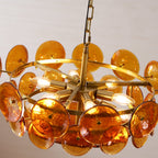 Close view from below of lit amber discs and candle-style bulbs on the brass arms of this Clérachic chandelier.
