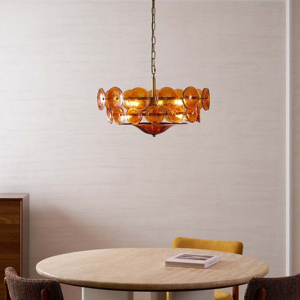 Amber Clérachic chandelier hung above a travertine-topped round table with a book and two chairs, against a pale wall.