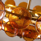 Close detail of amber glass discs with green brass studs and lit bulbs behind, on a Clérachic chandelier.