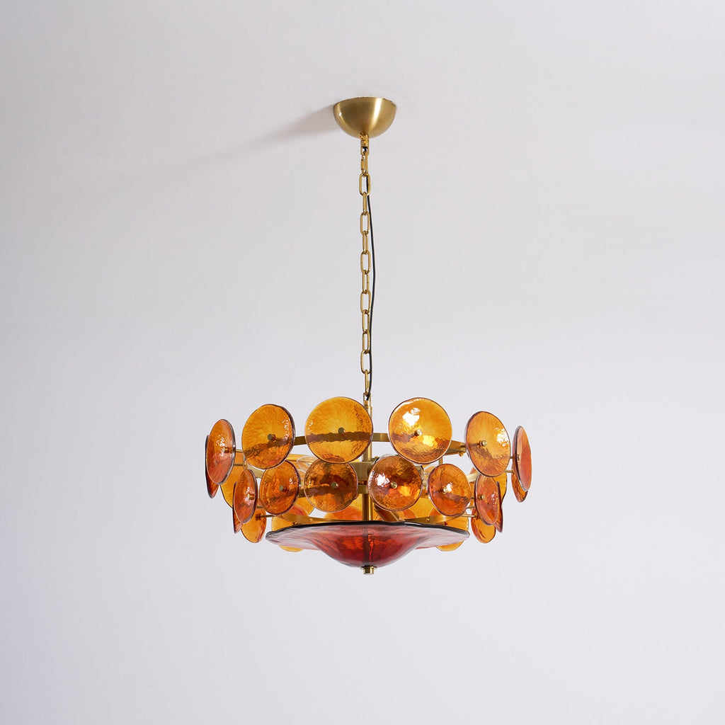 Amber glass disc chandelier from Clérachic, unlit, on a brass canopy and chain against a plain pale wall.