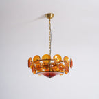 Amber glass disc chandelier from Clérachic, unlit, on a brass canopy and chain against a plain pale wall.