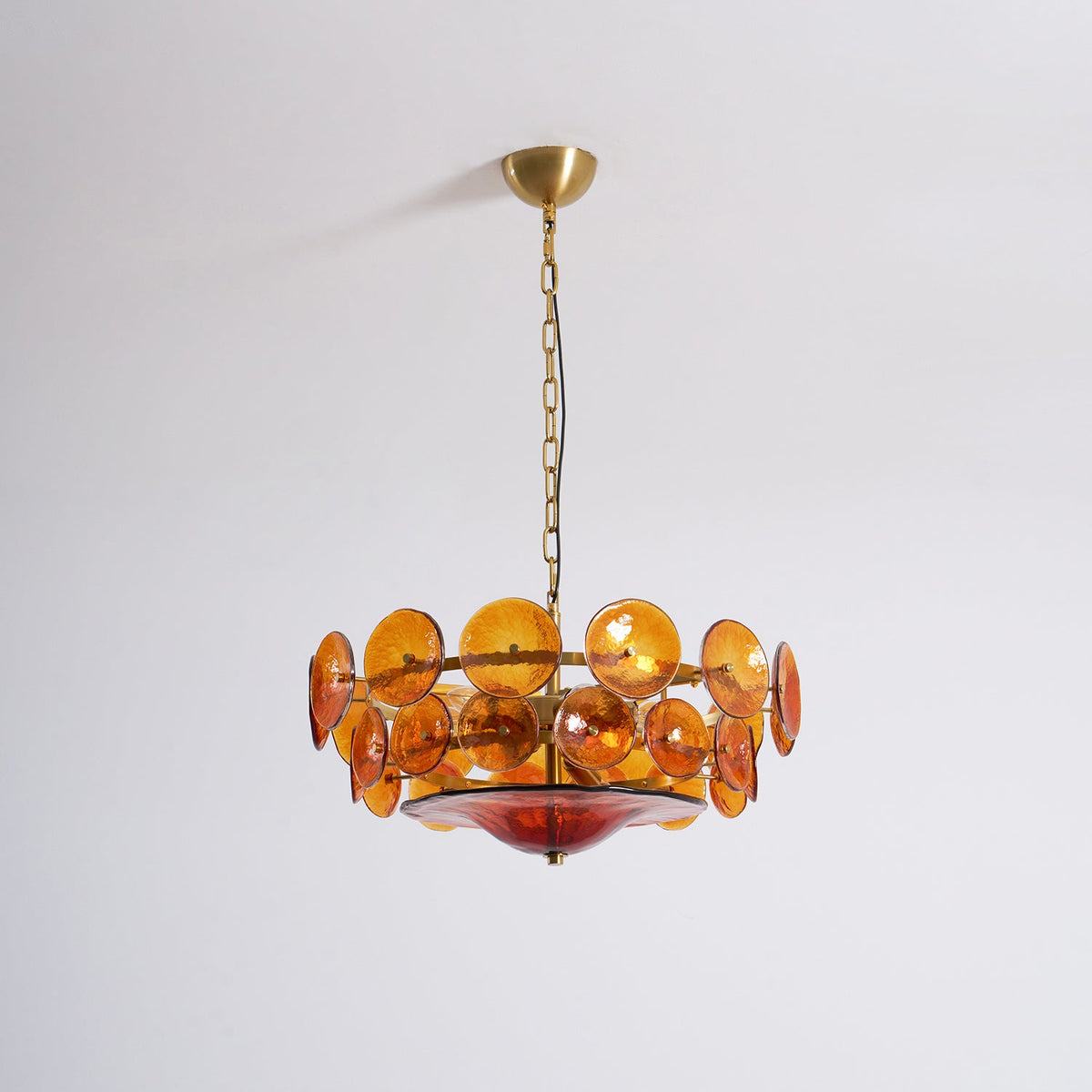 Amber glass disc chandelier from Clérachic, unlit, on a brass canopy and chain against a plain pale wall.
