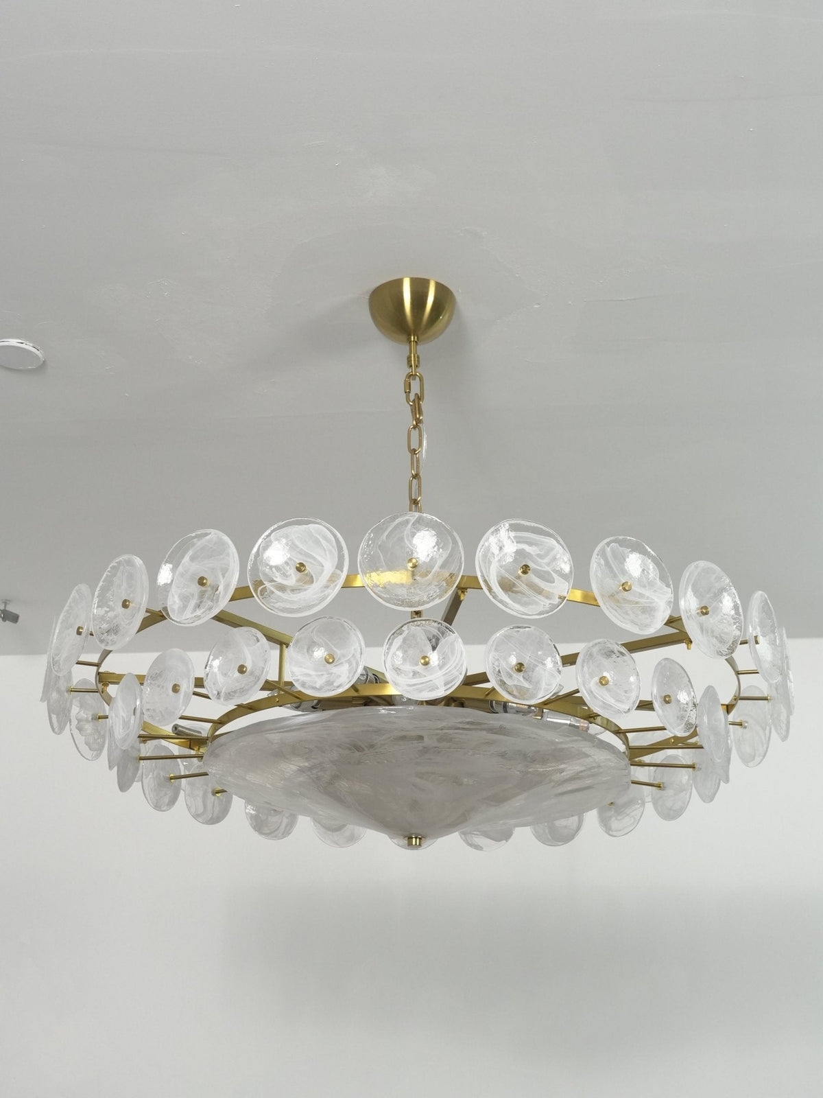 White frosted glass chandelier from Clérachic seen from below, with the wide glass bowl under two rings of discs and a brass canopy.