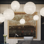 A group of this Clérachic pendant's white spheres in different sizes hang in front of a large landscape painting in a dark-panelled entrance.