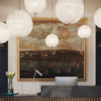 Close view of this Clérachic pendant's white spheres hanging in front of a gilt-framed painting above a stone reception desk.