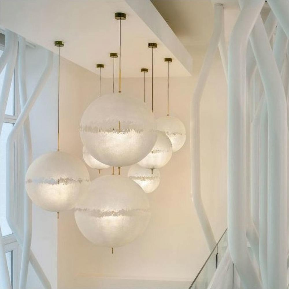 Cluster of six white spheres of this Clérachic pendant at different heights beside curving white balustrade supports in a bright stairwell.