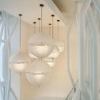 Cluster of six white spheres of this Clérachic pendant at different heights beside curving white balustrade supports in a bright stairwell.