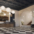 Spheres of this Clérachic pendant hang in a hall with a dark coffered ceiling, a chequered floor and a reception desk below.