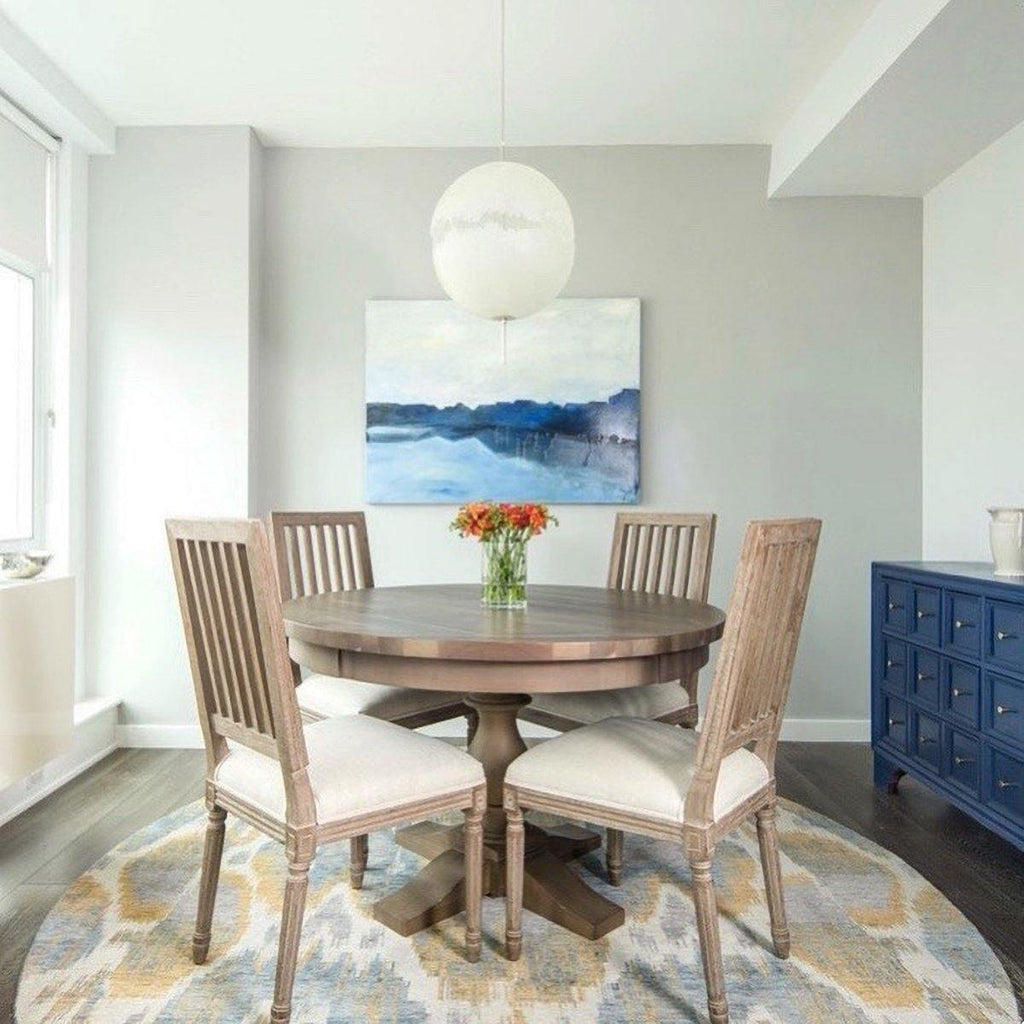 A single sphere from this Clérachic pendant hangs over a round wooden dining table and four chairs, with a blue abstract painting behind.