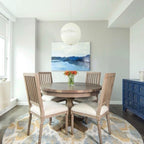 A single sphere from this Clérachic pendant hangs over a round wooden dining table and four chairs, with a blue abstract painting behind.
