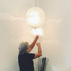 A person adjusts a hanging sphere from this Clérachic pendant on a pale wall, with a second dome-shaped shade just below.