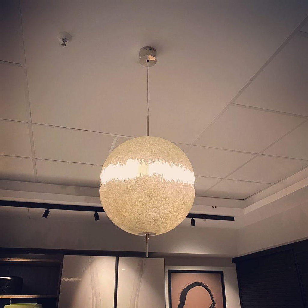 A lit sphere of this Clérachic pendant glows warm cream under a suspended ceiling with track spotlights.