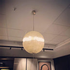 A lit sphere of this Clérachic pendant glows warm cream under a suspended ceiling with track spotlights.
