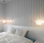 White sphere with a clear ragged band glowing above a bed, with a second sphere on the left, in a bedroom with a birch-pattern wall, shown on this Clérachic pendant.