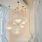 A cluster of this Clérachic pendant's spheres hangs from gold-toned stems in a bright stairwell beside white tree-like supports.
