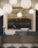 Large and small white spheres from this Clérachic pendant hang beside a painting and a reception desk, shown in a tall portrait view.