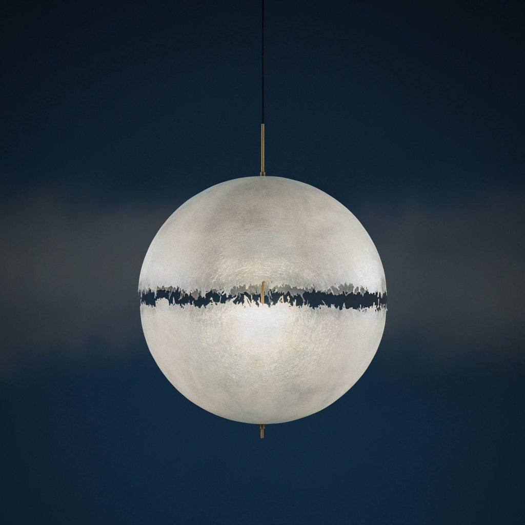 Pale sphere with a dark jagged band, this Clérachic pendant seen against a deep navy background in a studio-style shot.