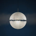 Pale sphere with a dark jagged band, this Clérachic pendant seen against a deep navy background in a studio-style shot.