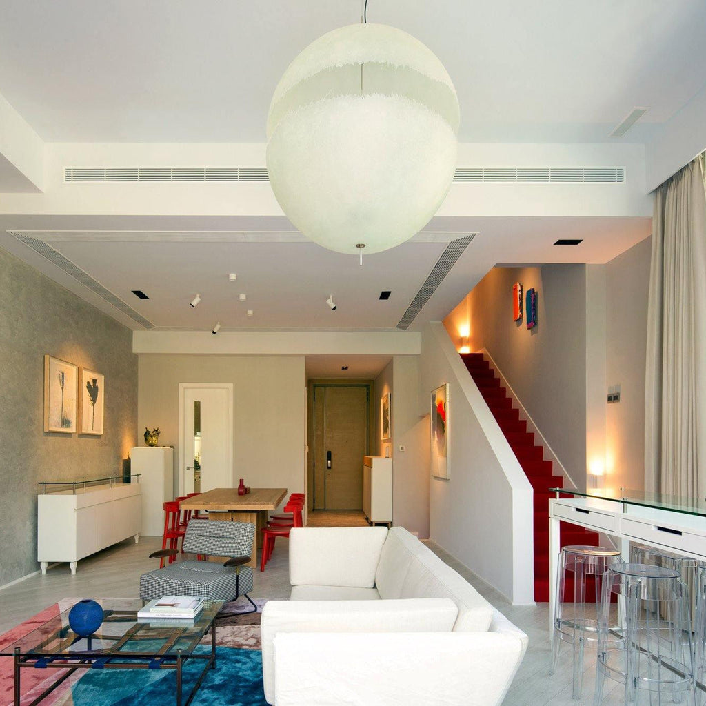 A large white sphere from this Clérachic pendant hangs close to the ceiling in a living space with a red-carpeted staircase beyond.