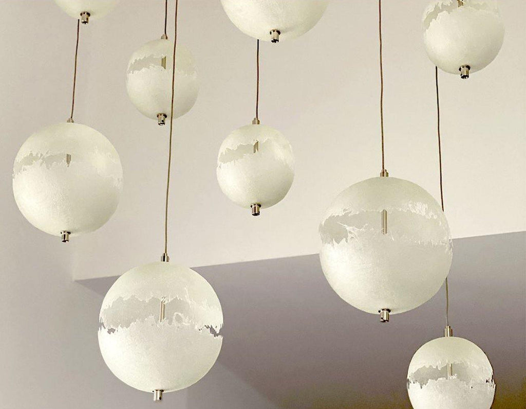 Looking up at a cluster of white spheres on thin cords, with a ragged cut-out band on each, from this Clérachic pendant.