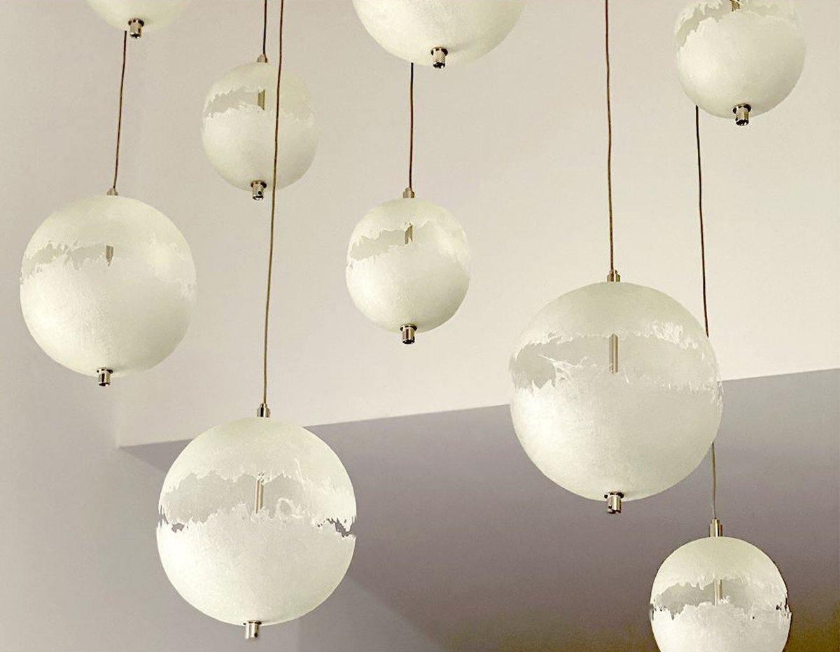Looking up at a cluster of white spheres on thin cords, with a ragged cut-out band on each, from this Clérachic pendant.