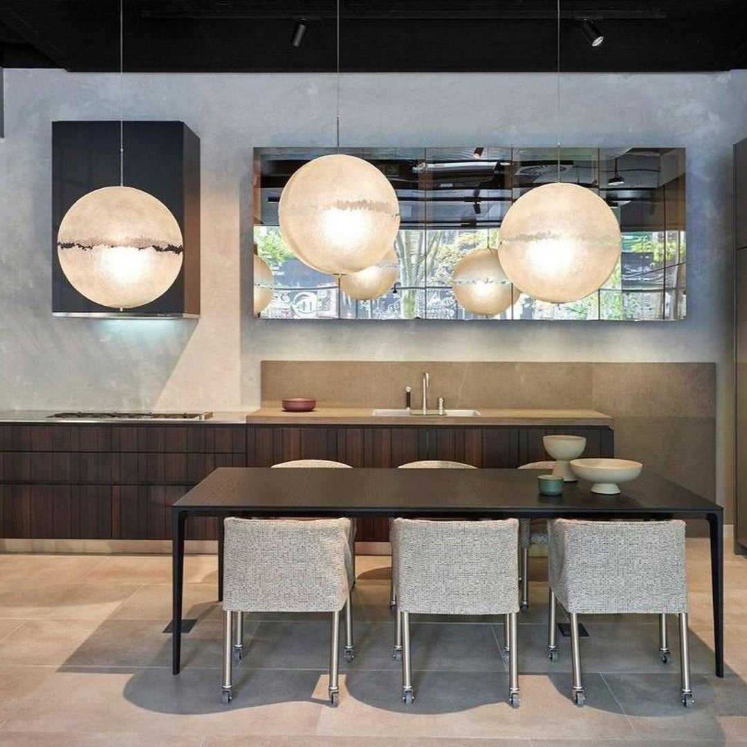 Three spheres of this Clérachic pendant glow in a modern kitchen and dining area with a dark table and mirror-fronted cabinets.