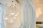 Wide view of this Clérachic pendant's spheres hanging in a bright stairwell near white tree-shaped supports and brass wall lights.