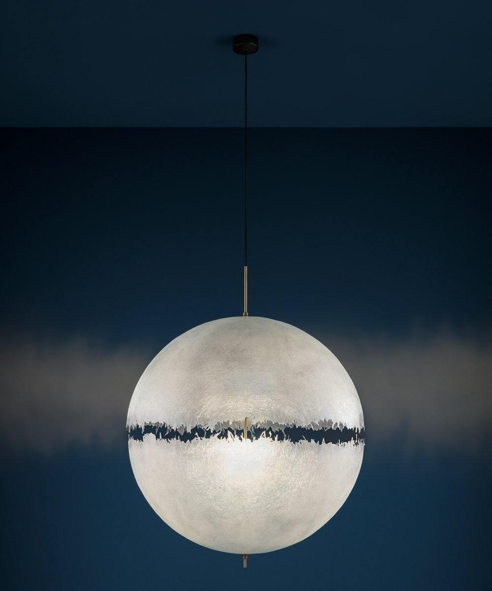 Same sphere from this Clérachic pendant with a soft glow on the navy wall behind, showing the dark band across its middle.