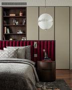 A white sphere of this Clérachic pendant hangs in a bedroom with a red padded headboard and a bookcase beside it.