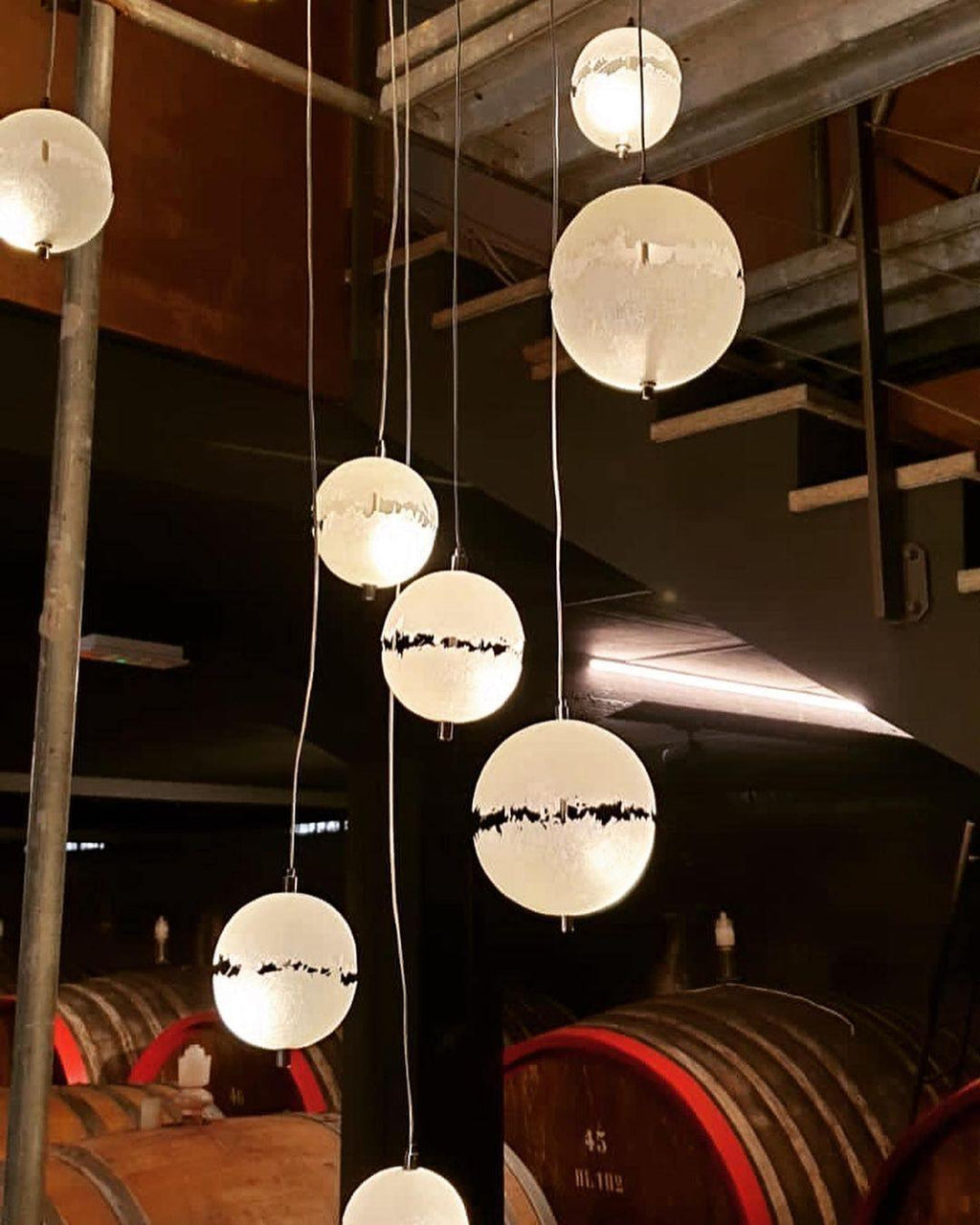 This Clérachic pendant's spheres glowing in a wine cellar stairwell above oak barrels on a dark floor.