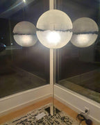 Three spheres of this Clérachic pendant glow behind a window at night, the centre one brightest, above a patterned rug.