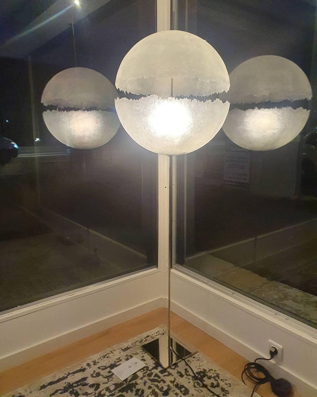 Three spheres of this Clérachic pendant glow behind a window at night, the centre one brightest, above a patterned rug.