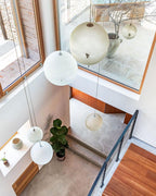 Three of this Clérachic pendant's spheres hang through a high stairwell with window light and a leafy plant below.