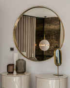 A single small sphere of this Clérachic pendant reflected in a round brass-framed mirror above two cream bedside drawers.