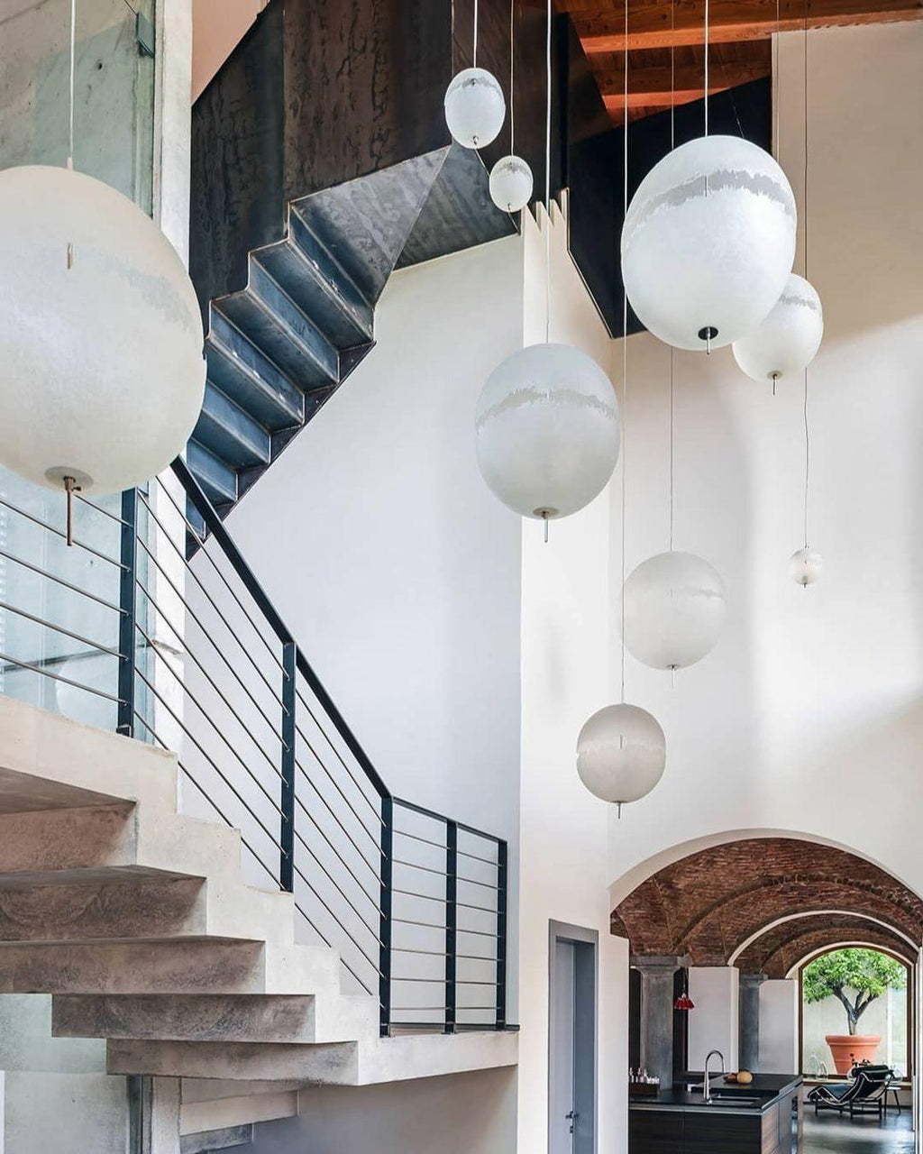 Spheres of this Clérachic pendant hang over a stairwell with concrete steps, a black steel railing and arches in the background.