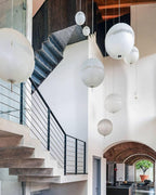 Spheres of this Clérachic pendant hang over a stairwell with concrete steps, a black steel railing and arches in the background.