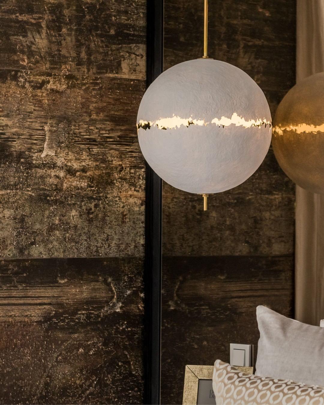 Close view of a sphere with a bright ragged band, from this Clérachic pendant, against a dark rough wall.
