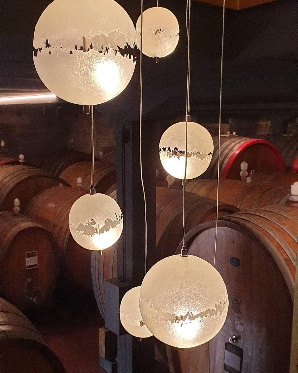 Spheres of this Clérachic pendant glowing among oak barrels in a cellar, with a bright band on each.