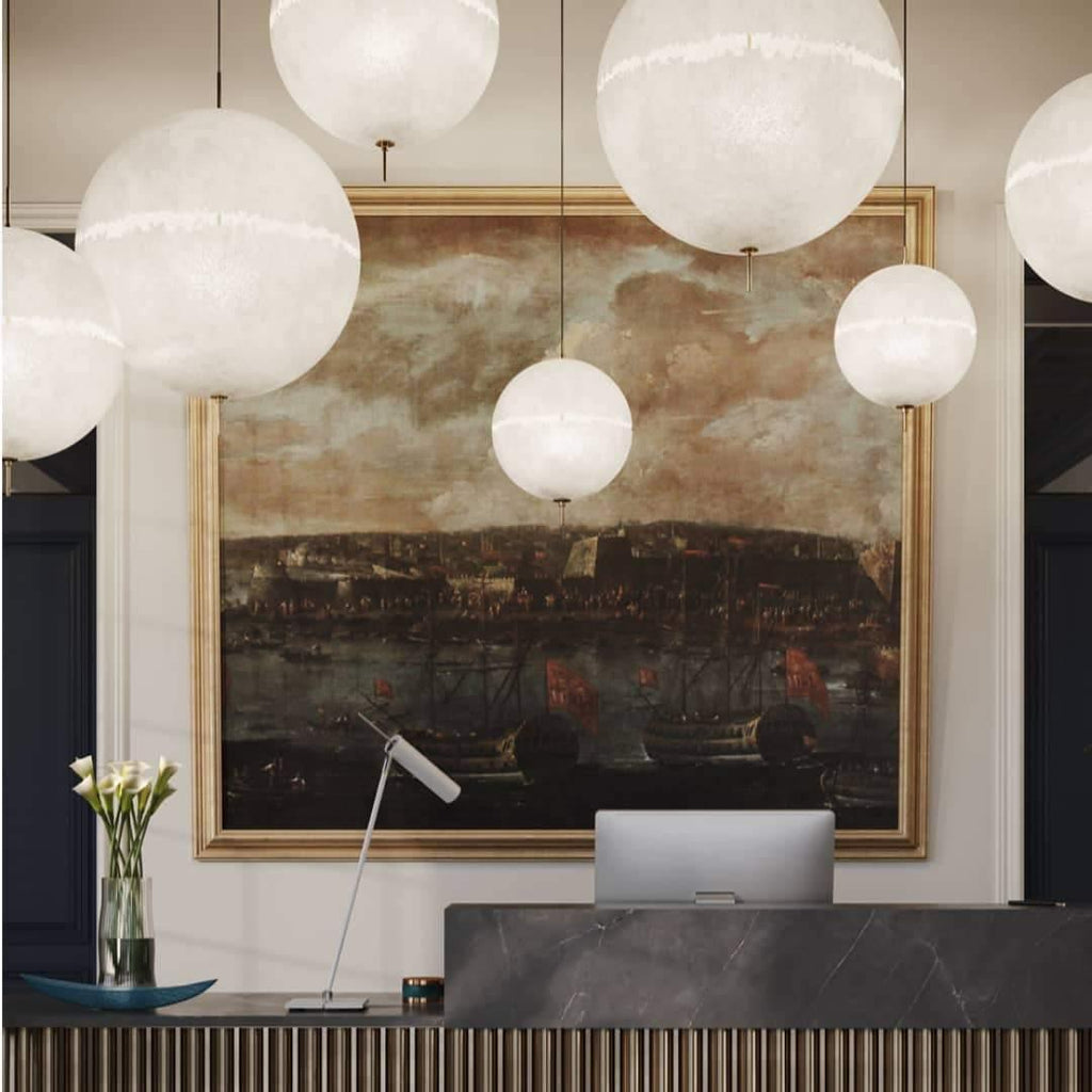 Spheres of different sizes hang in front of a gilt-framed painting, a close view of this Clérachic pendant above a reception desk.