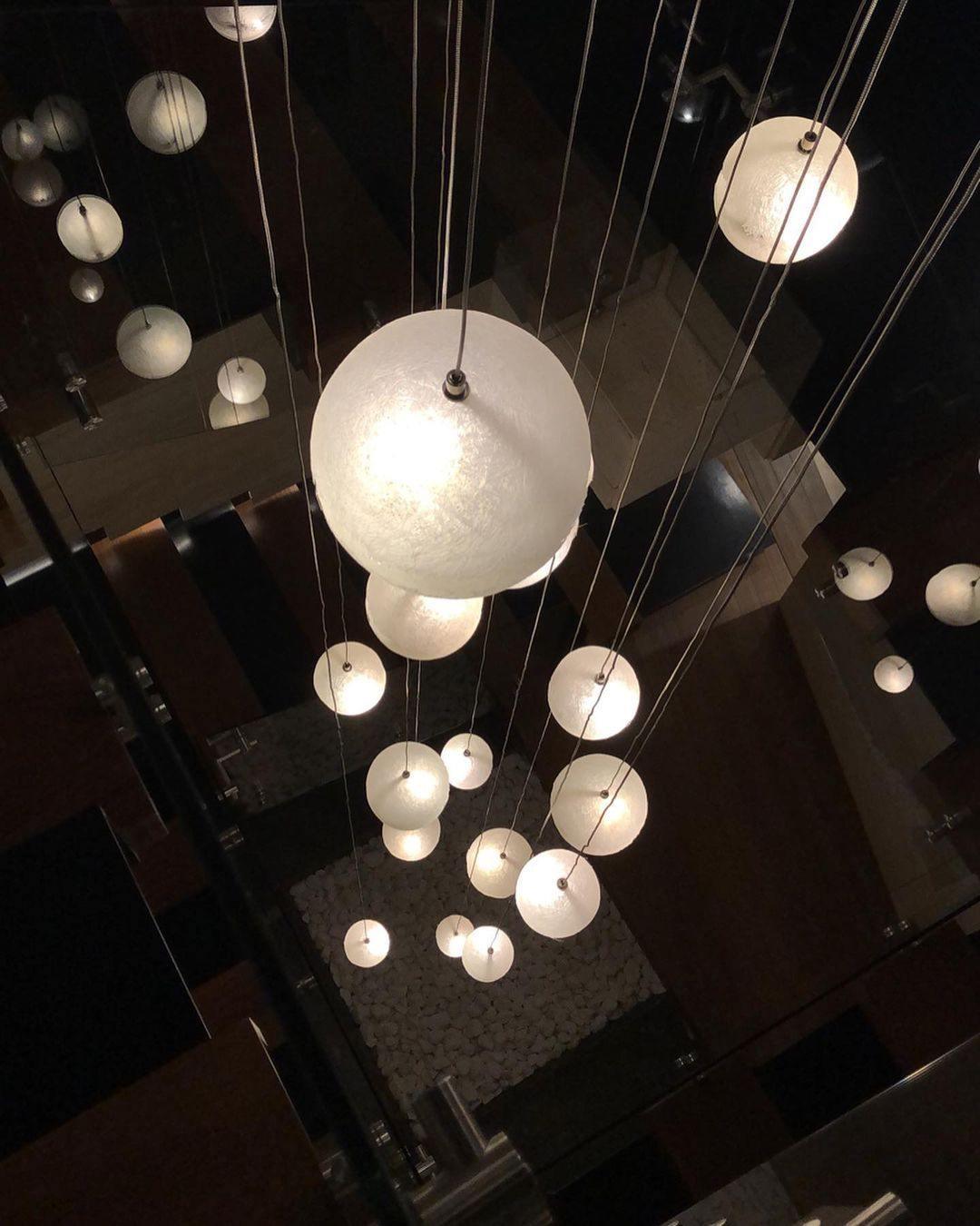 Looking down at a cascade of small and large glowing spheres on fine cords, this Clérachic pendant over a dark stairwell.