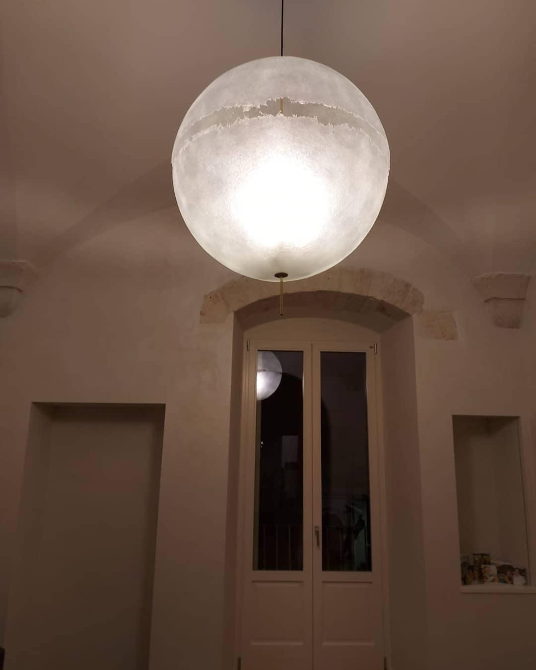 This Clérachic pendant hangs in a vaulted room with a pair of tall doors, its sphere glowing softly in the dim light.