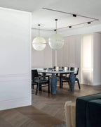 Two of this Clérachic pendant's spheres hang over a dark dining table in a white-panelled room with track lighting.