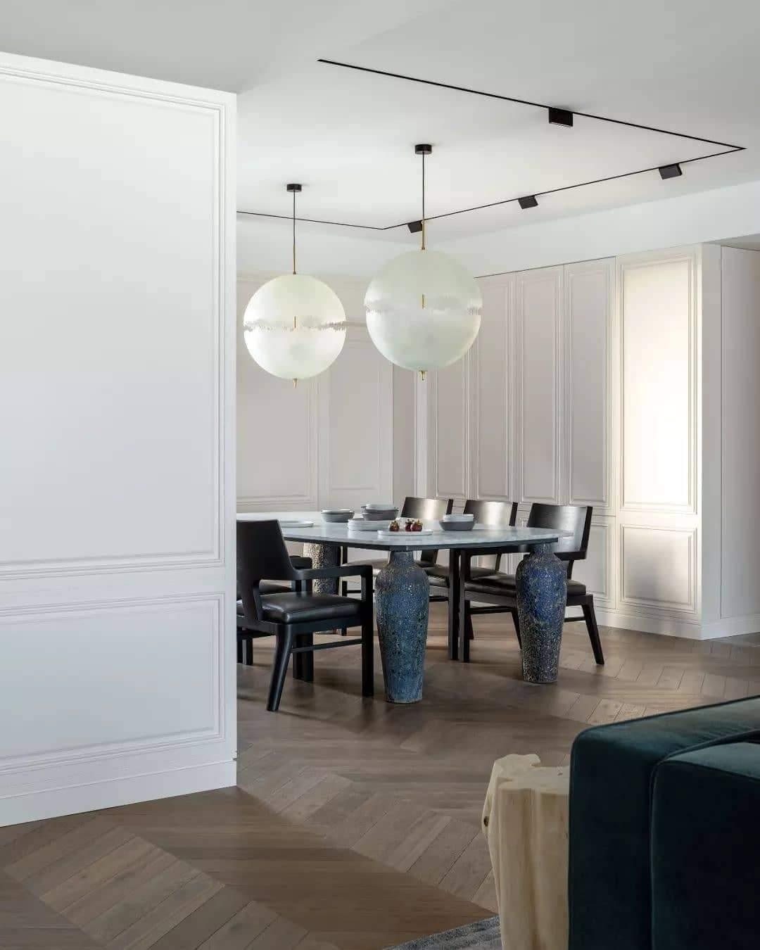 Two of this Clérachic pendant's spheres hang over a dark dining table in a white-panelled room with track lighting.