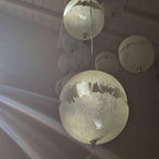 Close view of a sphere on this Clérachic pendant, its torn-edged clear band catching the light in a darker room.