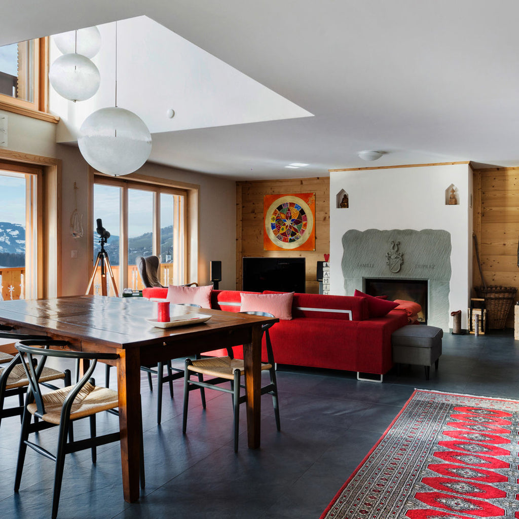 This Clérachic pendant hangs in an open-plan living room with a wooden table and a red sofa, beside a second sphere.